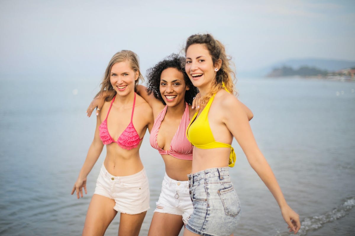 Photo of three smiling women in bikini tops and denim shorts 3756164